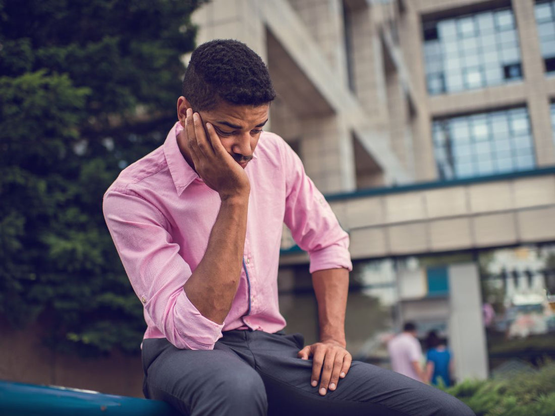 A man in a pink shirt sitting thoughtfully outside a modern building, representing the contemplation of combining CBG and THC.