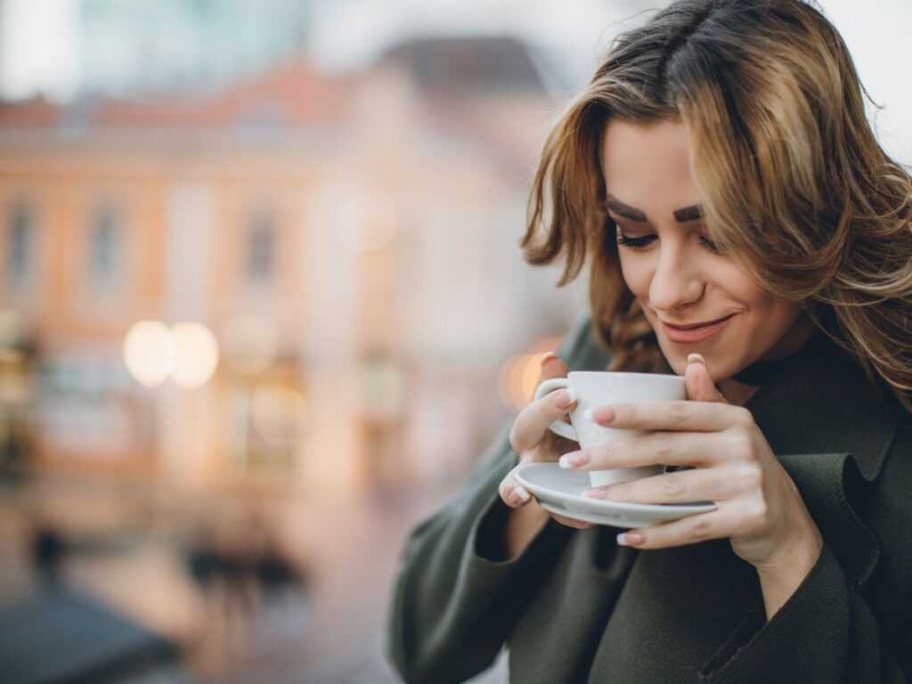 11 Proven Tips For Better Sleep 3 A woman smiling and drinking a hot cup of coffee